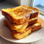 A tall stack of golden brown easy french toast slices drizzled with syrup and dusted with powdered sugar.