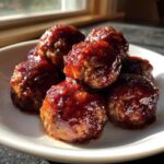 A serving of shiny, saucy grape jelly meatballs piled high on a small white plate.