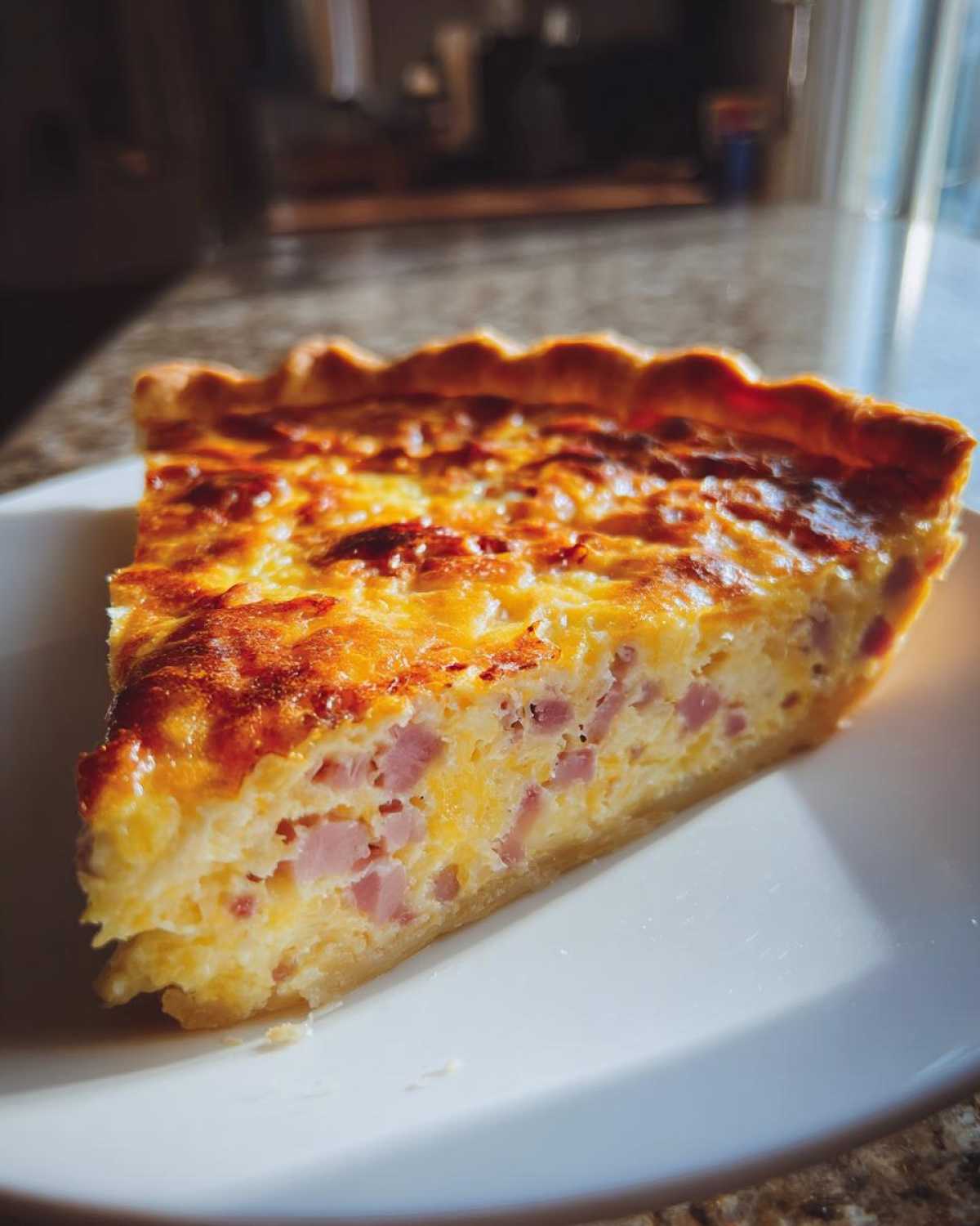 A close-up slice of golden-brown Ham and Cheese Quiche showing chunks of ham and melted cheese in the egg custard.