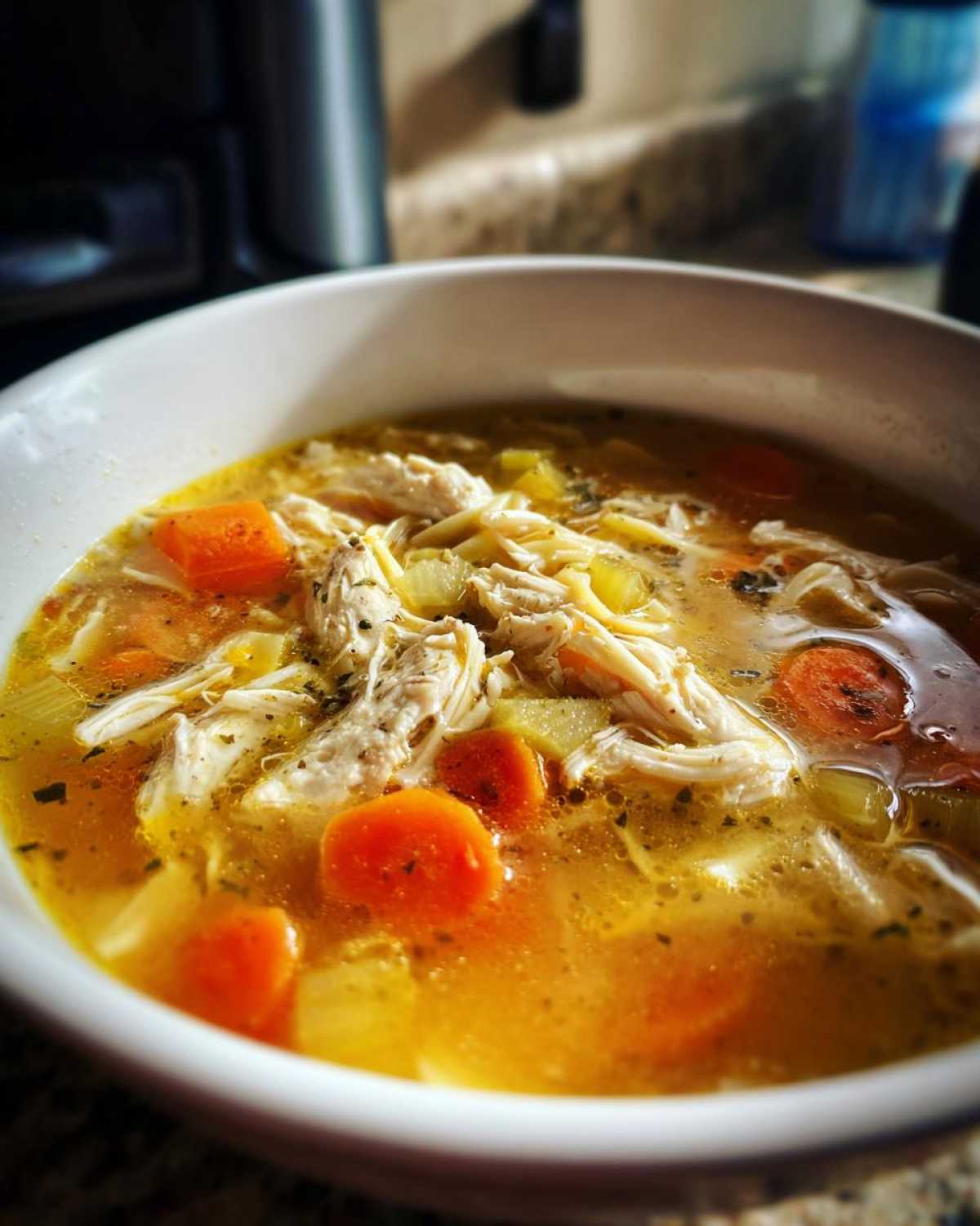 Close-up of a steaming white bowl filled with rich broth, shredded chicken, carrots, and noodles from the chicken noodle soup recipe.