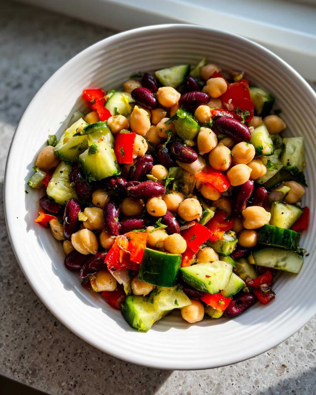 Close-up of a vibrant bowl of high protein bean salad featuring chickpeas, kidney beans, cucumber, and red pepper.
