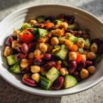 Close-up of a vibrant, high protein bean salad featuring chickpeas, kidney beans, cucumber, and tomatoes in a white bowl.
