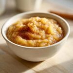 Close-up of chunky, homemade applesauce sprinkled with cinnamon, served in a small white bowl.