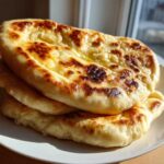A stack of three golden-brown, soft and chewy homemade naan bread pieces brushed with melted butter.