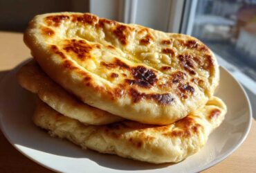 A stack of three golden-brown, soft and chewy homemade naan bread pieces brushed with melted butter.