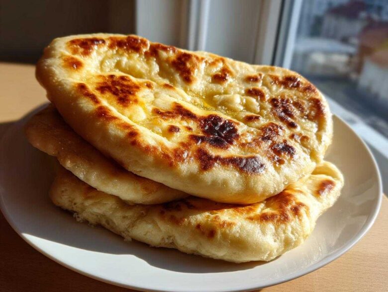 A stack of three golden-brown, soft and chewy homemade naan bread pieces brushed with melted butter.