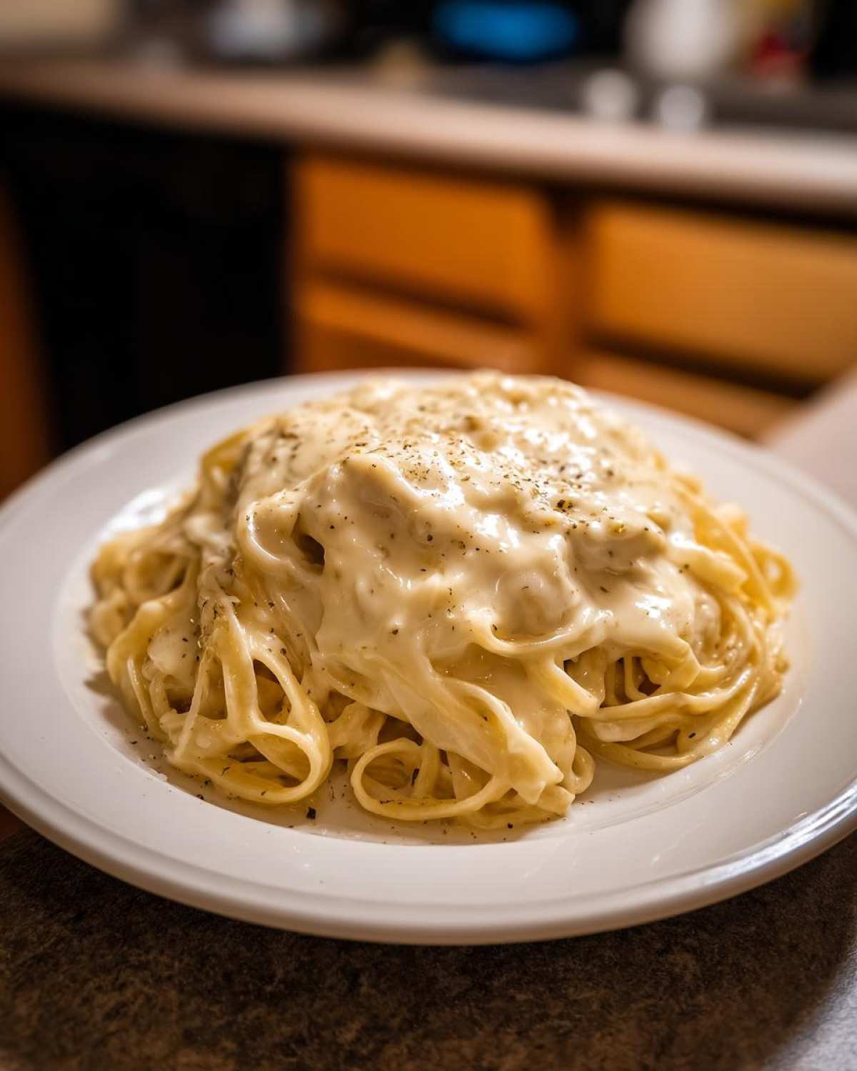 A close-up of fettuccine pasta generously coated in creamy homemade olive garden alfredo sauce and sprinkled with black pepper.