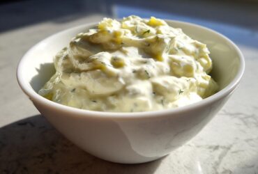 Close-up of creamy, chunky homemade tartar sauce recipe served in a small white bowl.
