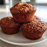 Three freshly baked, golden brown honey bran muffins stacked on a small white plate.