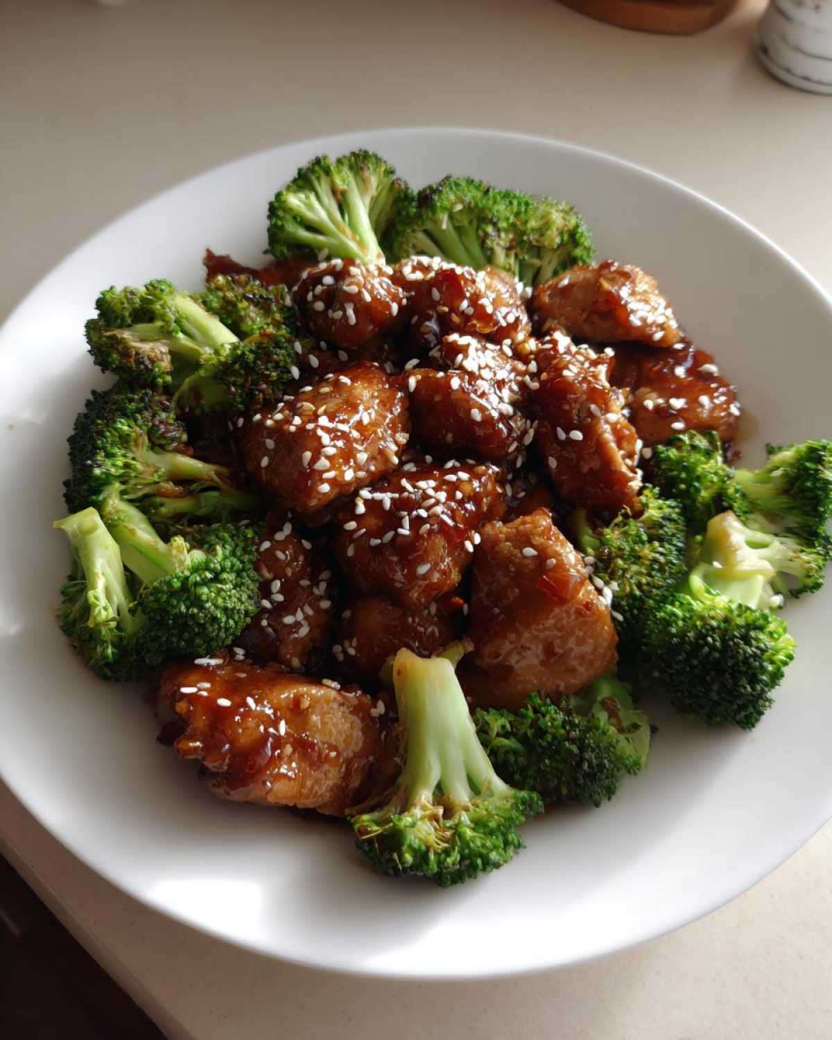Close-up of honey garlic chicken and broccoli pieces topped with sesame seeds on a white plate.