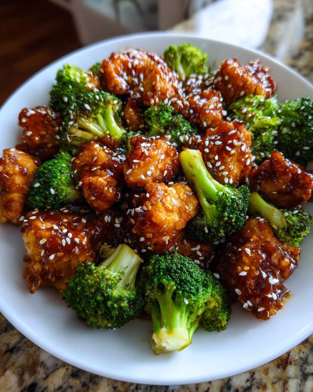Close-up of glazed honey garlic chicken and broccoli florets topped with white sesame seeds.