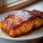 A perfectly cooked fillet of salmon coated in a shiny, dark honey garlic glaze, resting on a white plate.