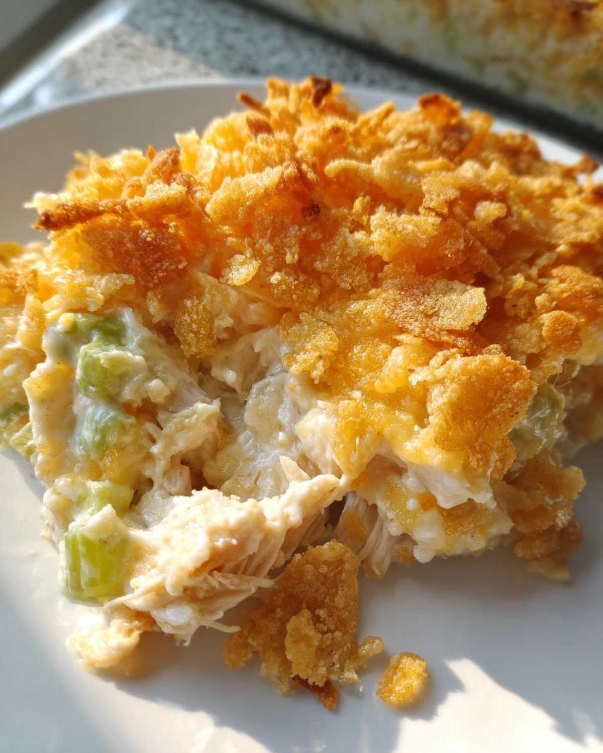 Close-up of a portion of hot chicken salad casserole topped with golden, crunchy cornflakes.