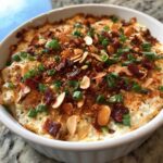 Close-up of a baked, creamy neiman marcus dip topped generously with bacon bits, sliced almonds, and chopped green onions.