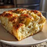 A thick, golden slice of Italian herb and cheese bread showing a cheesy, airy interior on a white plate.