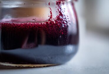 Close-up of dark purple elderberry syrup recipe liquid with vibrant red foam clinging to the inside of a small glass jar.
