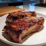 Close-up of two perfectly cooked, glazed pork steak recipe portions resting on a white plate.