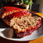 Close-up of a juicy meatloaf, sliced and covered in a thick, glossy red glaze.