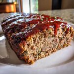 A thick slice of moist Keto meatloaf topped with a rich, shiny glaze and sprinkled with herbs.