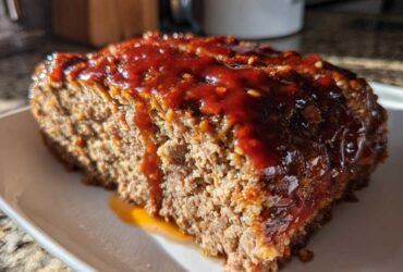 Close-up of a thick slice of moist Keto meatloaf topped with a shiny, dark red glaze.