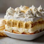 Close-up of a decadent layered banana pudding dessert topped with piped whipped cream and sliced bananas.