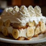 A decadent layered banana pudding dessert featuring vanilla wafers, sliced bananas, and topped with swirls of whipped cream.