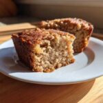 Two moist squares of homemade applesauce cake sitting on a small white plate, highlighted by sunlight.