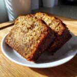 Two moist slices of rich brown applesauce cake resting on a small white plate.