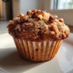 Close-up of a single, moist banana nut muffin topped with brown sugar crumble and chopped pecans.