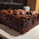 Close-up of a rich, dark slice of black bean brownies topped with melted chocolate chips on a white plate.