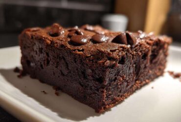 Close-up of a rich, dark slice of black bean brownies topped with melted chocolate chips on a white plate.