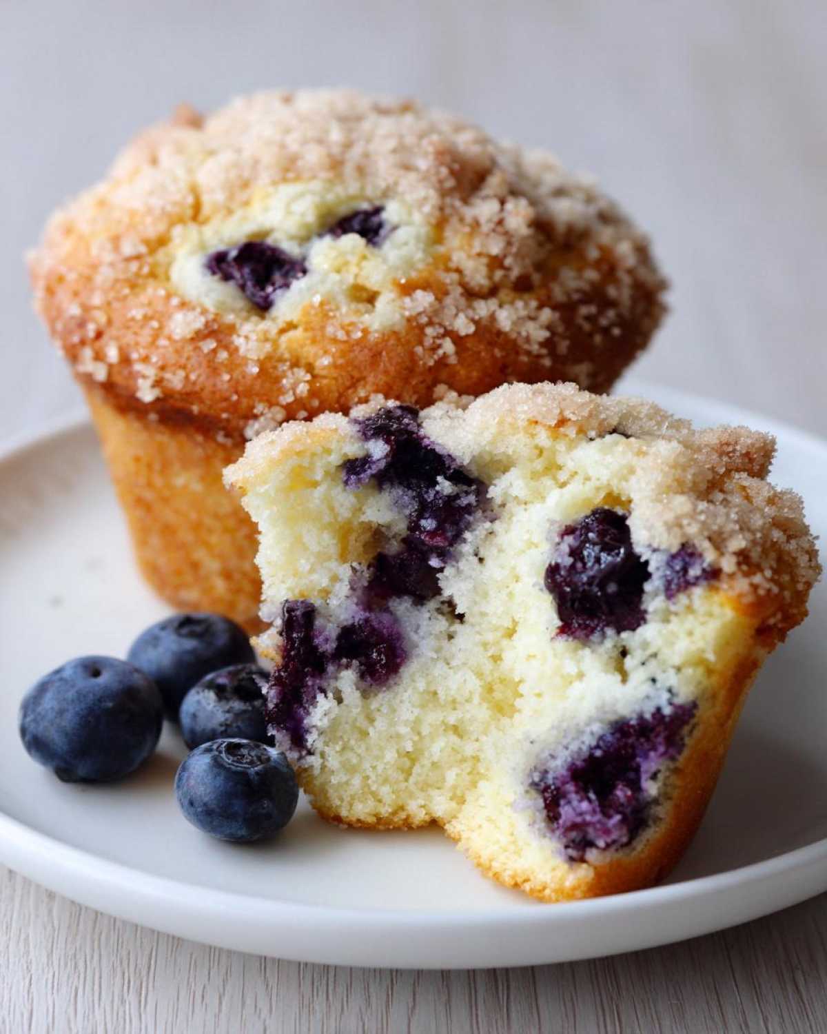 A close-up of a delicious blueberry muffin cut in half, showing the moist interior packed with blueberries, next to a whole muffin.