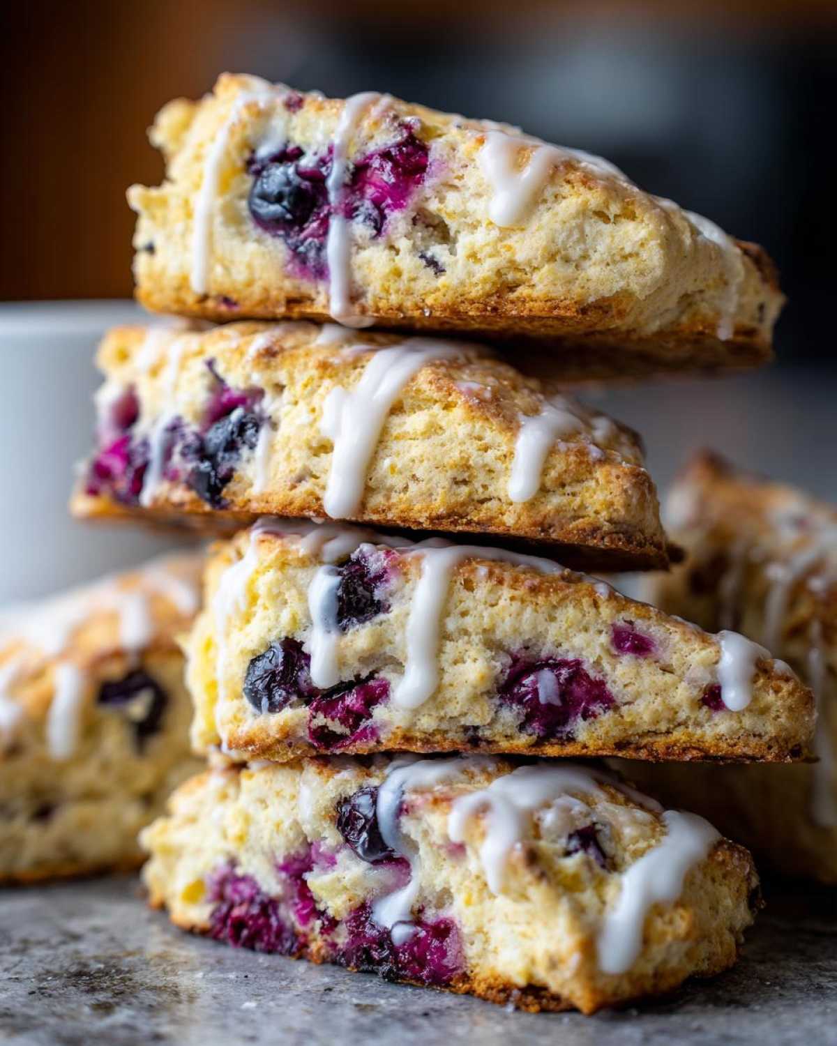 Close-up of a stack of four moist blueberry scones drizzled with white vanilla glaze.