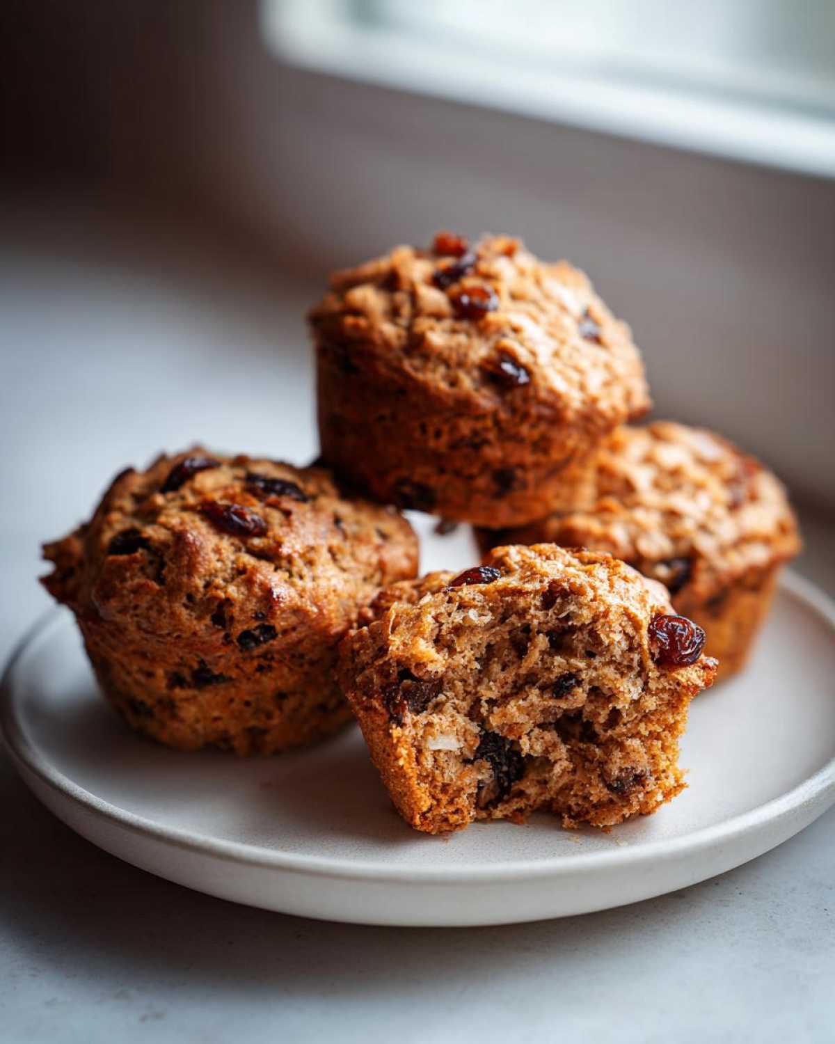Close-up of several moist bran muffins, one broken open to show the texture and raisins inside.