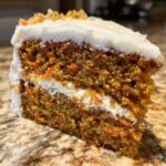 Close-up of a moist slice of carrot cake recipe showing two layers of cake and cream cheese frosting.