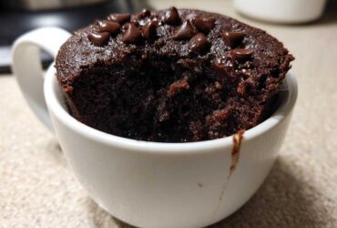Close-up of a rich, dark chocolate mug cake topped with chocolate chips, with a bite taken out.