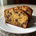 Two thick slices of moist date nut bread, rich with dark fruit pieces, served on a white plate.