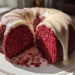 A moist red velvet bundt cake cut open, showing the deep red interior and thick white cream cheese glaze dripping down the sides.
