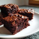 Close-up of fudgy sweet potato brownies stacked on a white plate, topped with melted chocolate chips.