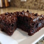Two rich, dark chocolate sweet potato brownies topped with melted chocolate chips on a white plate.