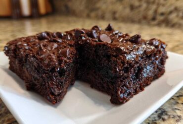 Two rich, dark chocolate sweet potato brownies topped with melted chocolate chips on a white plate.