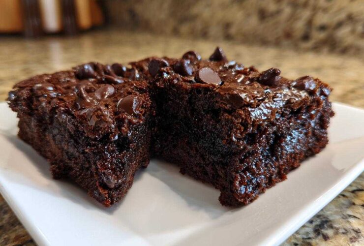 Two rich, dark chocolate sweet potato brownies topped with melted chocolate chips on a white plate.