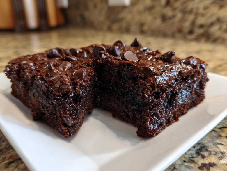 Two rich, dark chocolate sweet potato brownies topped with melted chocolate chips on a white plate.