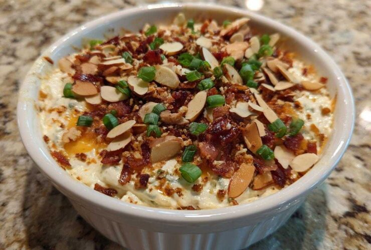 Close-up of a white bowl filled with creamy Neiman Marcus Dip, topped generously with bacon bits, sliced almonds, and green onions.
