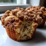 Close-up of a delicious oatmeal muffins with a thick, sugary cinnamon crumb topping, one muffin is partially eaten.