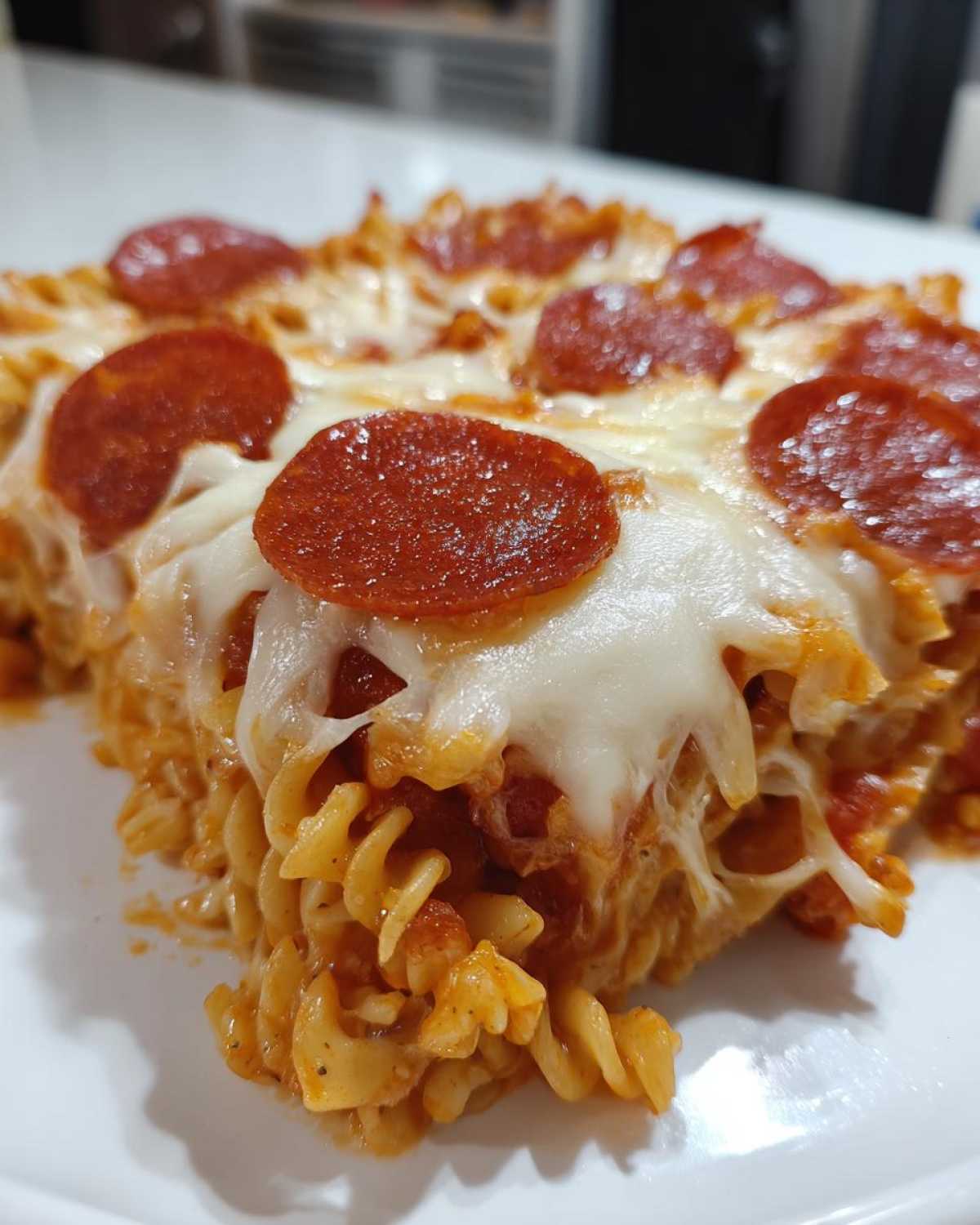 A close-up of a serving of baked pizza pasta topped with melted mozzarella cheese and slices of pepperoni.