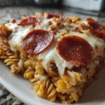 Close-up of a serving of baked pizza pasta featuring rotini noodles, melted mozzarella, and pepperoni slices.
