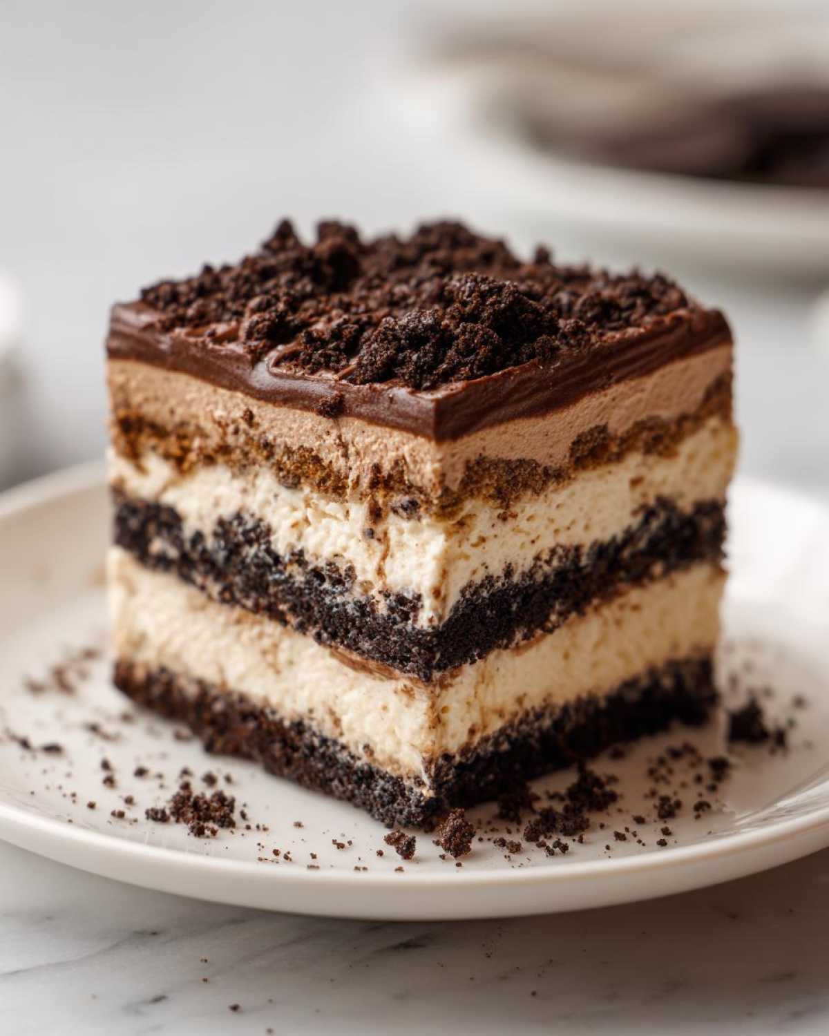 A layered square slice of Oreo dirt cake featuring cream, chocolate pudding, and crushed cookie layers.