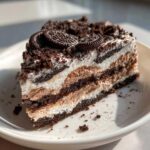 A decadent slice of layered Oreo dirt cake showing alternating layers of cream, mousse, and crushed cookies, topped with whole Oreos.
