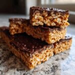 A stack of rich peanut butter rice krispie treats topped with a layer of bumpy melted chocolate.